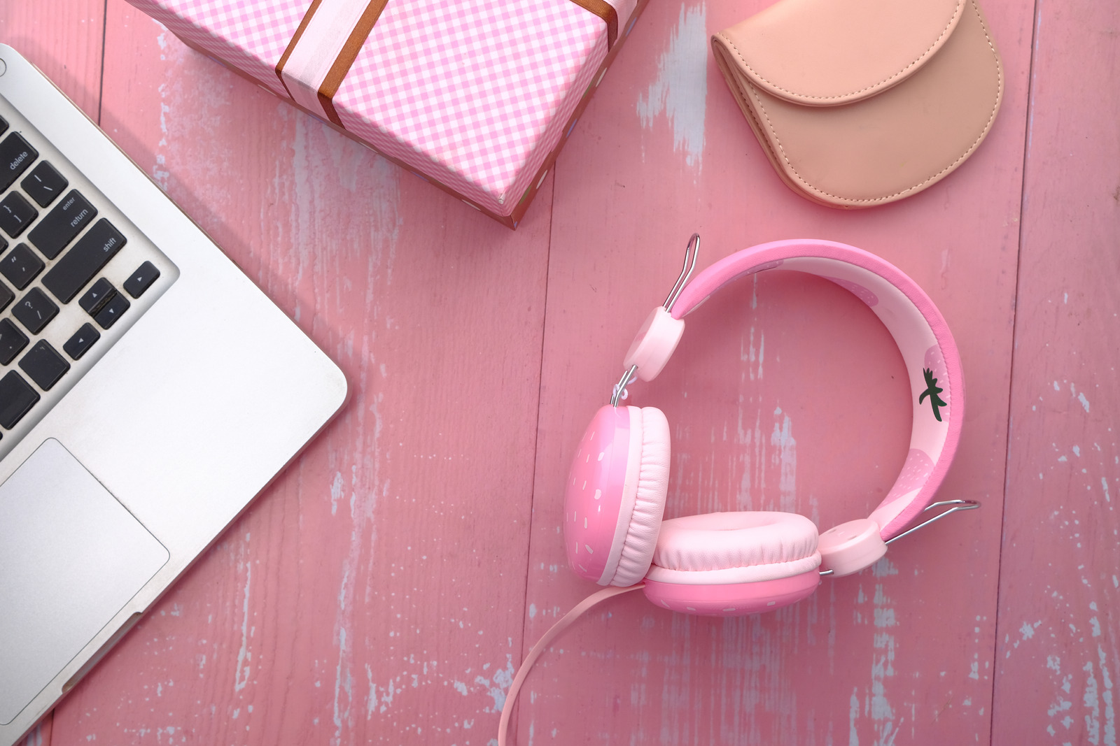 Pink headphones on a pink desk next to a laptop.